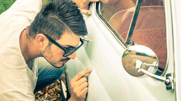 Man looking at paint chip on the side of a car.