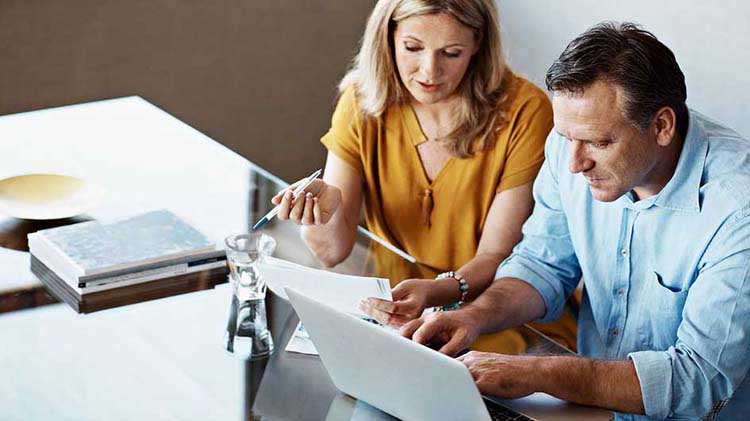 Woman and man with papers and a laptop discussing their retirement.