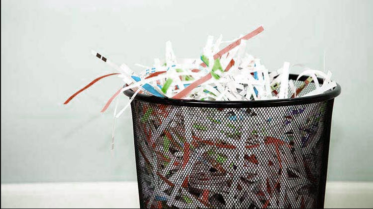 Black waste basket full of shredded paper.