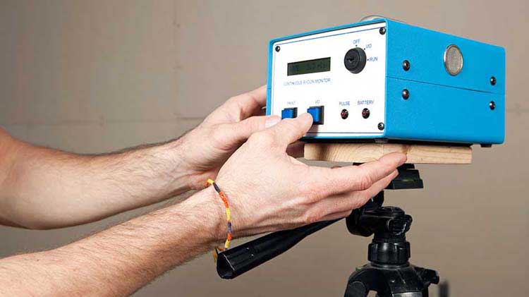 Man with a thin string bracelet pushing a button on a radon detector.