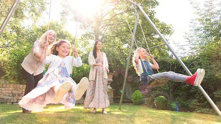 Two moms pushing kids on a swing set.