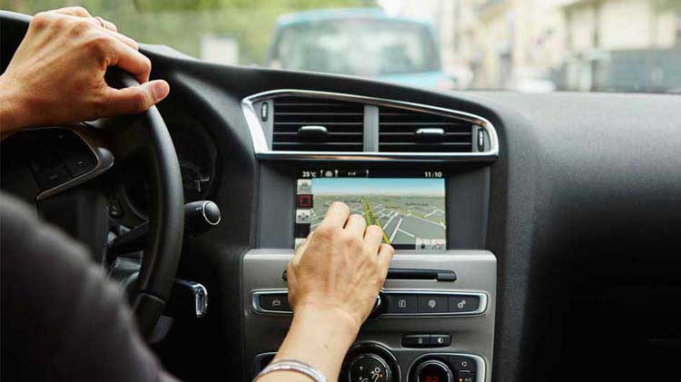 Person in a vehicle, one hand on the steering wheel and one interacting with an onboard telematics device.