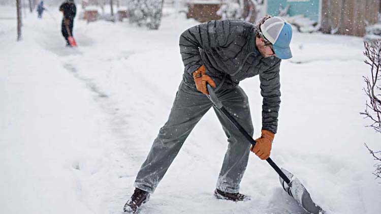 Business owner shoveling snow to clear a sidewalk in order to prevent slip and falls in the workplace.