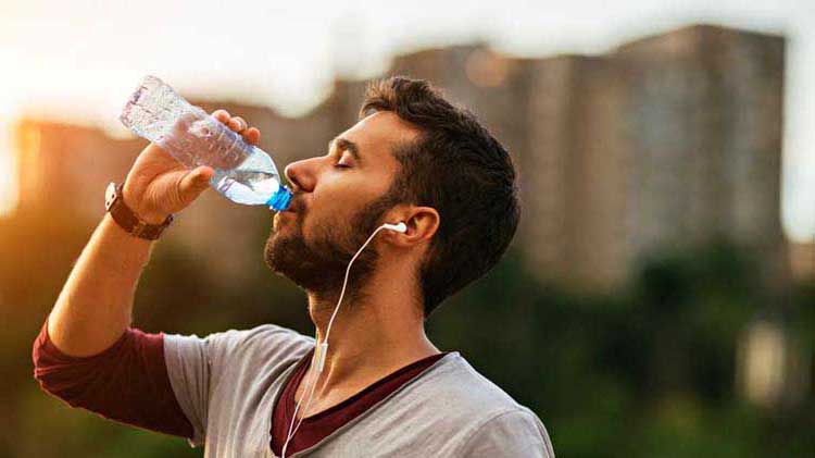 Athletic man drinking water on a humid day to help avoid heat illnesses.