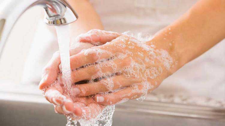 Person washing hands with soap bubbles under a running faucet.