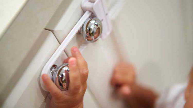 Child's hand on cabinet knob with a safety latch.