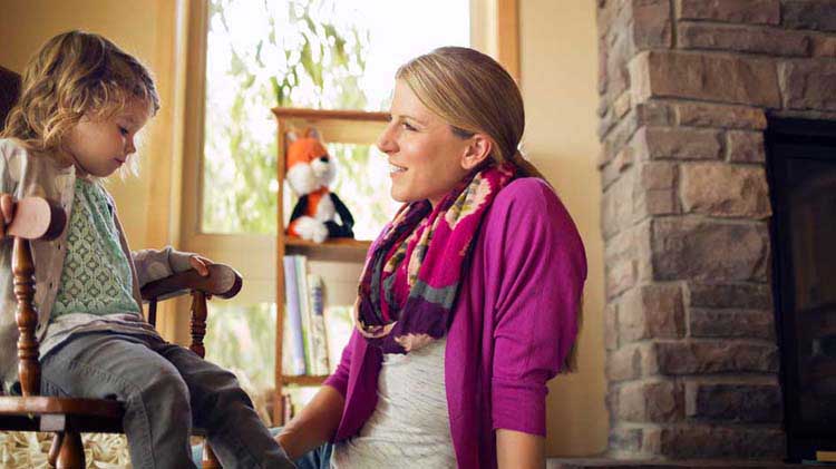 A mother and daughter chat while the daughter sits in a rocking chair.