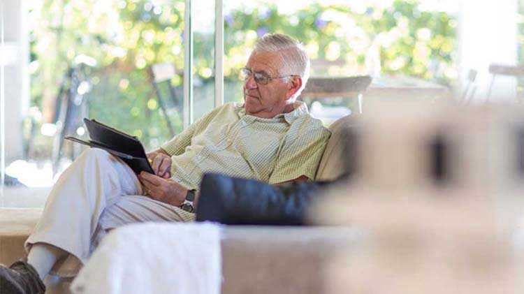 Older gentleman sitting in his arm chair reading about retirement savings.