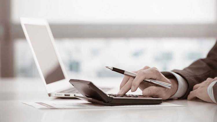 Person's hand operating a calculator next to a laptop