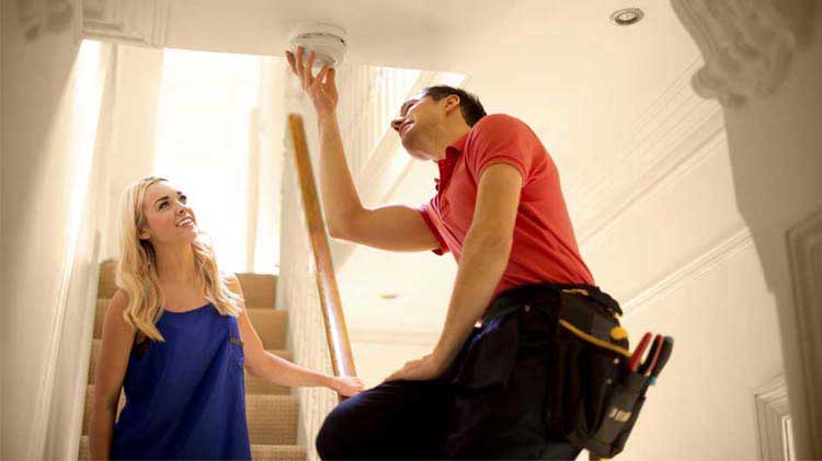 Woman watching man install a smoke detector.