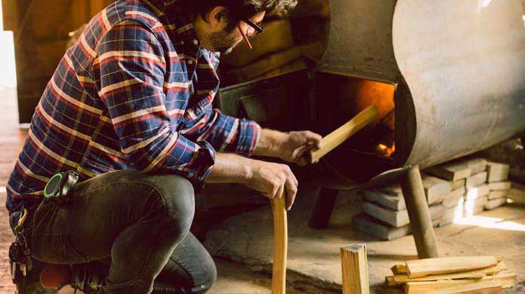 Man placing firewood in a wood stove.