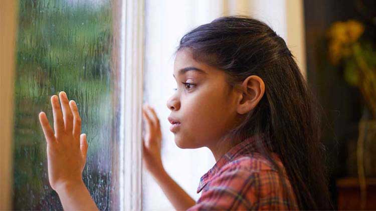 Young girl looking out a storm window.