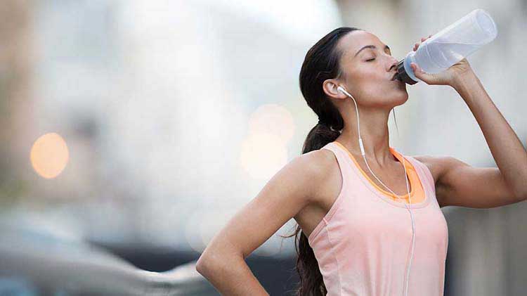 Woman drinking from a water bottle to help prevent a heat related illness.