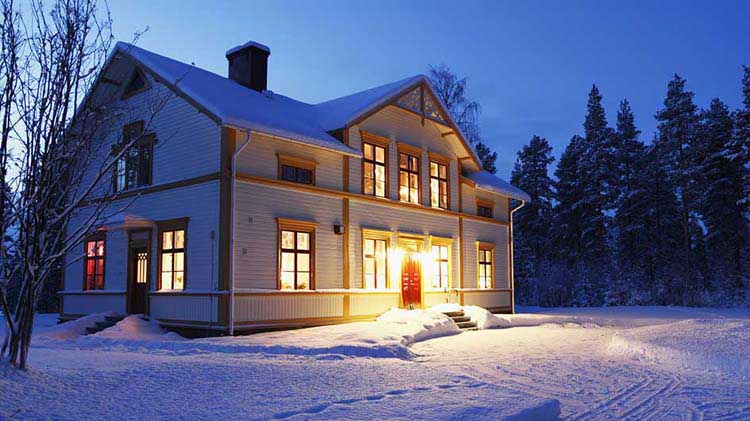 A well-lit house at dusk in a snowy landscape