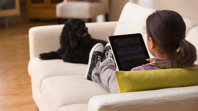 Child alone on couch looking at a tablet.