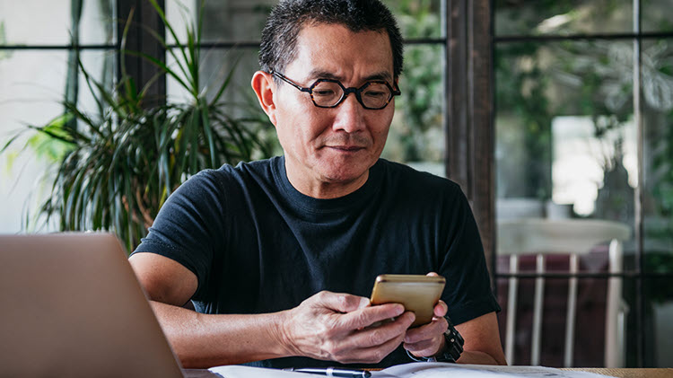 Man working at his home computer and checking is phone.