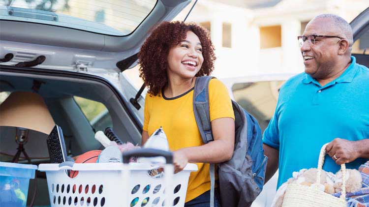 Young woman, preparing for college, loading a laundry basket of items into a car with her father.