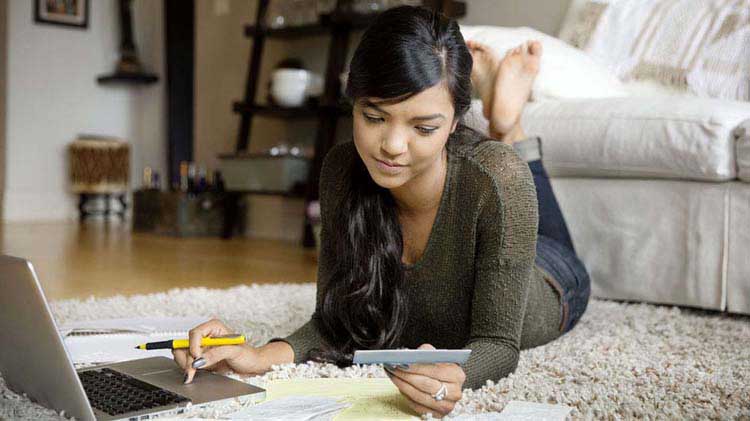 Girl laying on the floor paying bills.