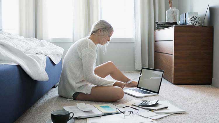 Woman searches through paperwork and on her laptop for a new apartment.