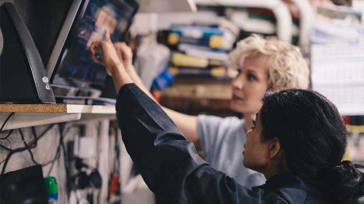 Two woman pointing at a monitor to better understand questions for the mechanic.