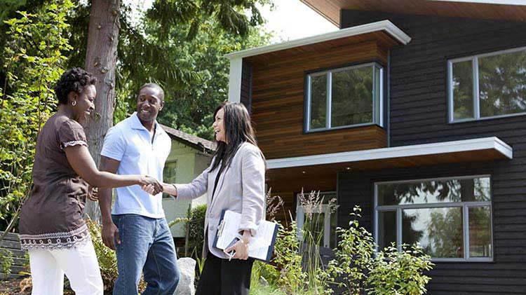  A man and a woman in front of their new house shaking hands with their realtor.