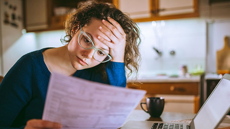 Woman at home reading paperwork at kitchen table trying to figure out how to pay her rent