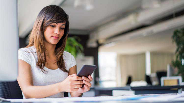 Woman sits at a table using her cell phone.