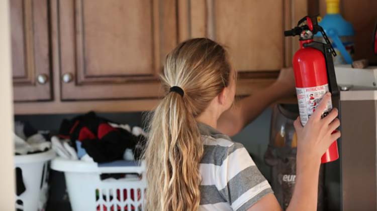 Girl putting fire extinguisher in laundry cabinet.