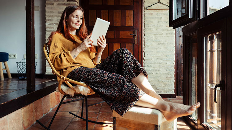 Woman sitting in a chair and researching how to improve financial wellness on her tablet.