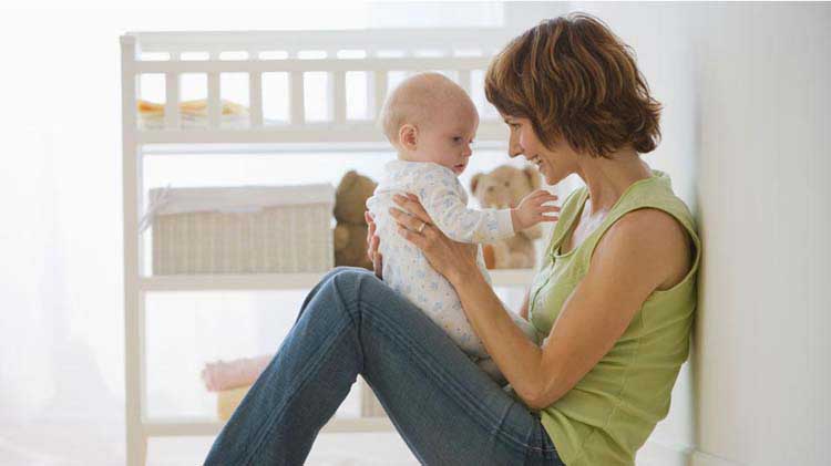 Mom sitting on the floor smiling and holding her baby