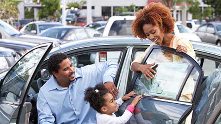 A family is looking at a used car on a dealership lot.