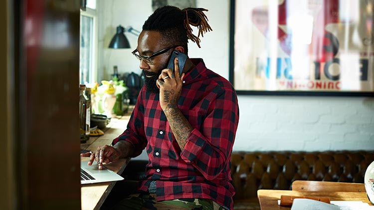 Adult man working on his laptop while also on the phone.