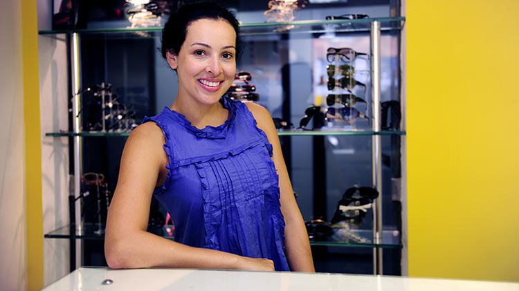 A small business owner stands at the counter in her sunglasses shop.