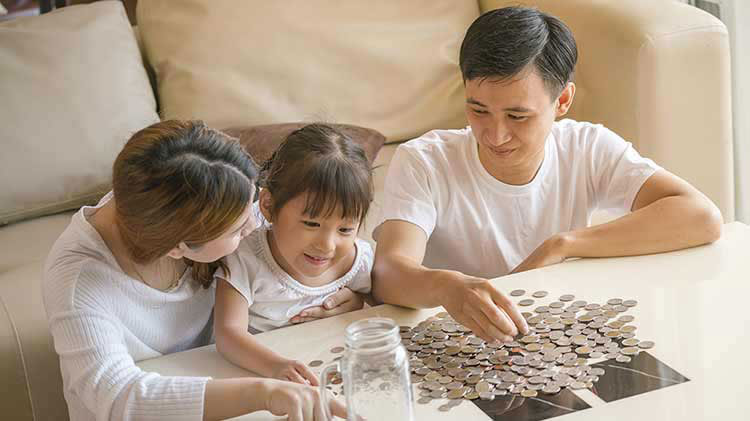 Family of three sitting around a table with coins poured out from a jar.