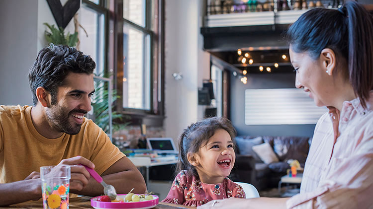 A mother and father sit at the table feeding their young daughter.