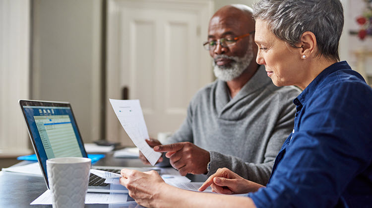 Man and woman look over paperwork and a computer, considering their estate plan.