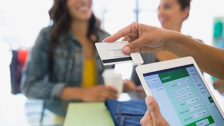 Alguien que sostiene una tableta y realiza un pago con tarjeta de crédito móvil en una tienda