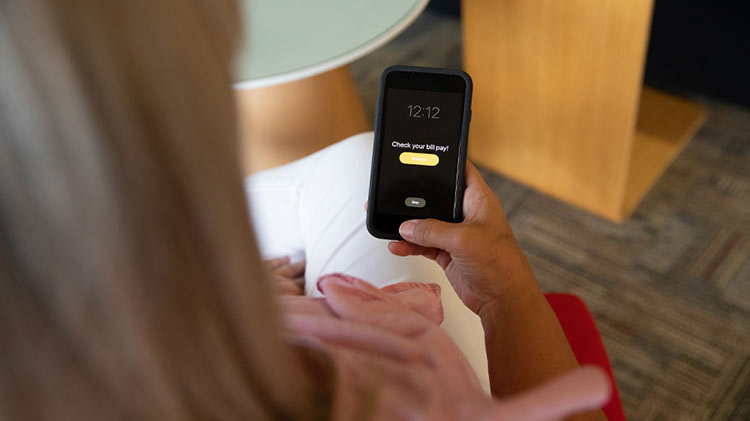 Woman sits looking at her mobile phone deciding if she should enroll in AutoPay.