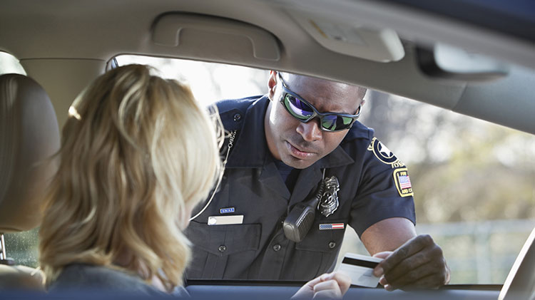 A young woman is pulled over in her car and a police man is talking to her as she hands him her drivers license.