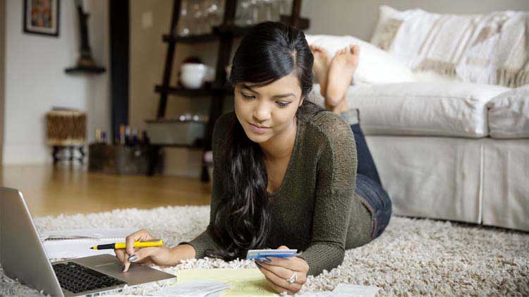 Woman laying on the floor paying bills on laptop.