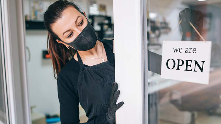 A woman wears a face mask while opening up her business