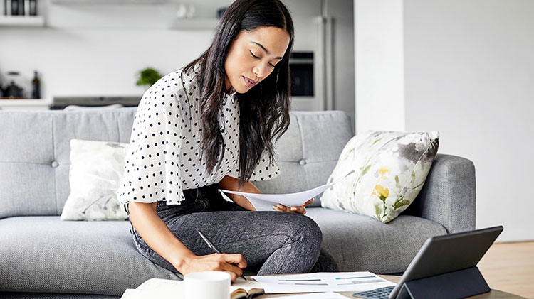 A young lady sits on her couch working on college loan paperwork.