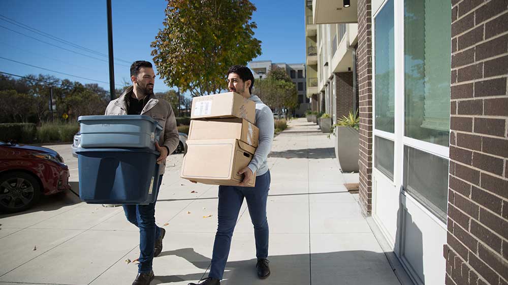 Two men carrying boxes from a building.