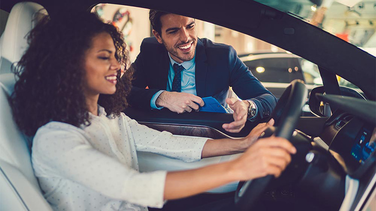 Woman considering buying a car while salesman leans in the window.