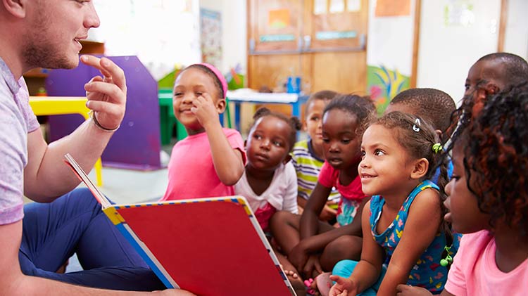 A man is volunteering in a classroom and reading to children.