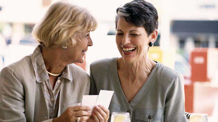 Two older women having a happy conversation while looking at cards.