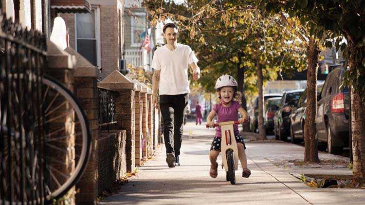 Father watching his young child ride a bike and considering the importance of life insurance.