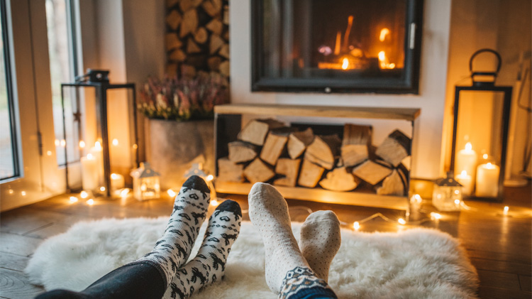 A couple in socks sit and enjoy their fireplace.