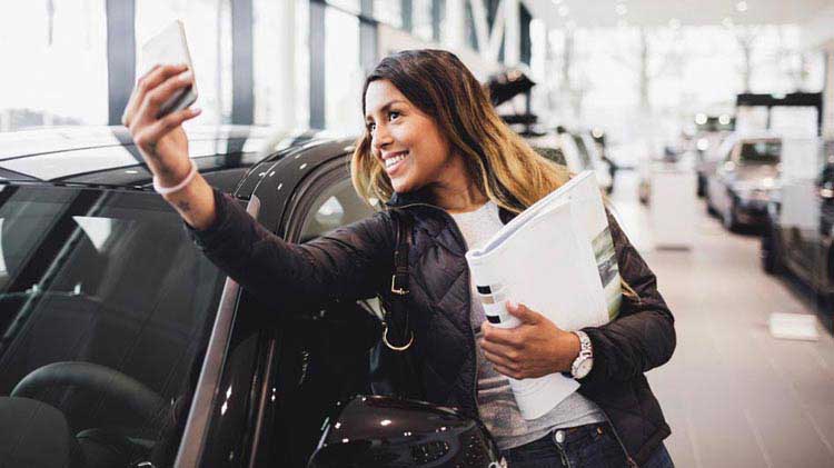 Woman taking a photo of herself with her new car purchase.