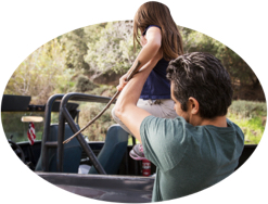 A father guides his daughter into a back-seat safety restraint